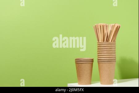 Tasses en carton et bâtonnets en bois sur une table blanche, fond vert. Vaisselle écologique Banque D'Images