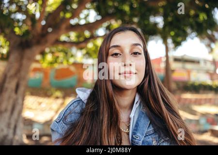 Brunette adolescente regardant l'appareil photo en toute confiance. Adolescent insouciant portant une veste en denim à l'extérieur de la ville. Jeune femme assise seule Banque D'Images