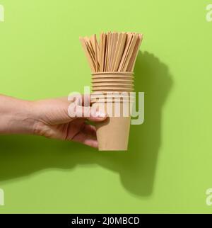 Tenir à la main les gobelets en carton brun et les bâtonnets en bois sur fond vert Banque D'Images