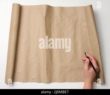 La main femelle tient un crayon de bois sur un rouleau de papier brun sur une table blanche. Place pour écrire du texte, liste Banque D'Images