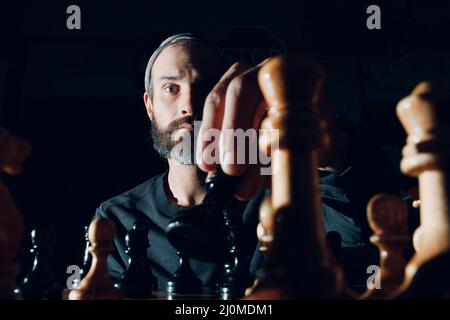 Jeune adulte beau homme jouant aux échecs dans l'obscurité avec le côté éclairé Banque D'Images