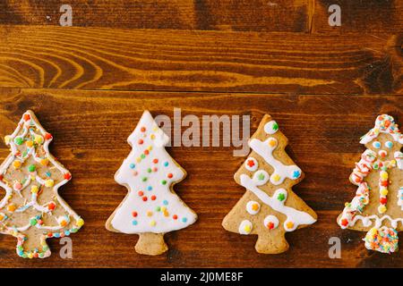 Quatre biscuits au pain d'épice en forme d'arbres de Noël, décorés de glace et de saupoudriers. Banque D'Images