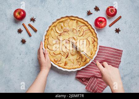 Mains de femmes avec couteau coupant la tarte aux pommes avec remplissage de crème aigre sur fond clair, vue du dessus. Banque D'Images