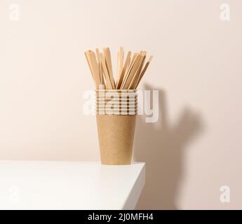 Tasses en carton et bâtonnets en bois sur une table blanche, fond beige. Vaisselle écologique, sans gaspillage Banque D'Images