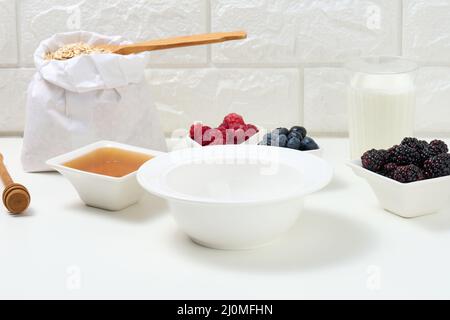 Videz la plaque de céramique blanche ronde, les flocons d'avoine et les fruits pour cuire le porridge sur une table blanche Banque D'Images