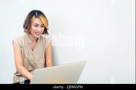 Femme asiatique, freelance avec cheveux courts tendance regardant l'écran tout en travaillant avec ordinateur portable sur fond blanc mur avec espace de copie. Banque D'Images