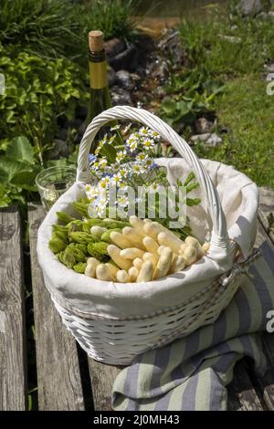 Asperges fraîches blanches et vertes crues offertes en gros plan dans un panier extérieur à un pont en bois Banque D'Images