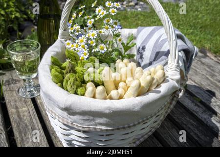 Asperges fraîches, blanches et vertes, offertes en gros plan dans un panier à l'extérieur, à un pont en bois Banque D'Images