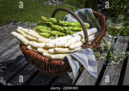 Asperges fraîches blanches et vertes crues offertes en gros plan dans un panier extérieur à un pont en bois Banque D'Images