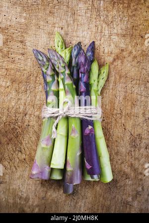 Bouquet d'asperges vertes et violettes, vue de dessus sur un panneau en bois rustique avec espace copie Banque D'Images