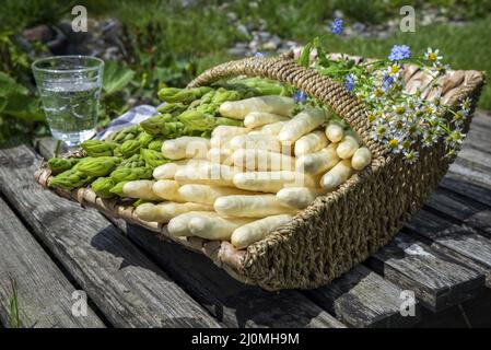 Asperges fraîches blanches et vertes crues offertes en gros plan dans un panier extérieur à un pont en bois Banque D'Images