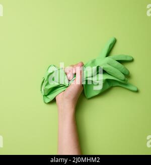 La main femelle tient des gants en caoutchouc vert pour le nettoyage sur fond vert. Une partie de la benne est soulevée Banque D'Images