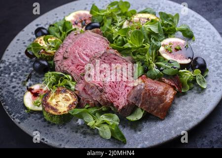 Des medaillons de filet de bœuf angus frits et vieux de style moderne accompagnés de légumes et d'agneaux de laitue servis sur un modèle nordique Banque D'Images