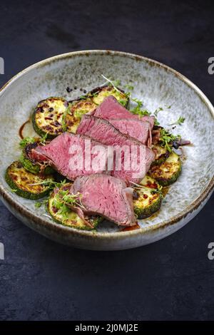 Medaillons de filet de bœuf angus frits et vieux, de style moderne, accompagnés de courgettes et de cresson, servis en gros plan dans un cadre nordique Banque D'Images
