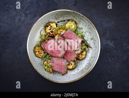 Des medaillons de filet de bœuf angus frits et séchés de style moderne accompagnés de courgettes et de cresson servis dans un bol de style nordique Banque D'Images