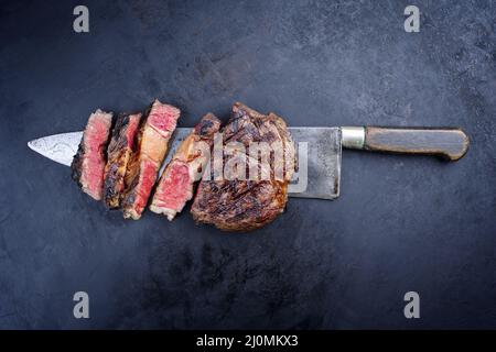 Grillades traditionnelles de bœuf Wagyu vieilli sec tranché et servi comme vue de dessus sur un grand couteau rustique sur un tableau noir W Banque D'Images