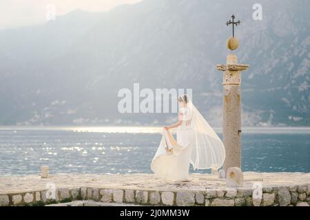 Mariée dans une longue robe blanche et un voile flottant dans le vent marche le long de l'île de Gospa od Skrpela Banque D'Images