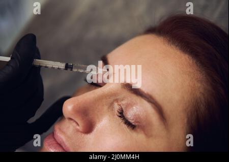 Gros plan de belle femme d'âge moyen obtenant des injections de beauté sur son front dans la clinique de cosmétologie de spa de bien-être. Injection de toxine botulinique et hy Banque D'Images