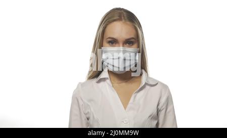 Une infirmière blonde dans un masque médical regarde directement dans l'appareil photo sur fond blanc. Jeune femme avec soulagement enlève le masque. Le concept est en Banque D'Images
