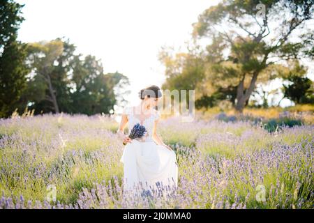 Sibenik, Croatie - 05.06.17: Mariée dans une robe de dentelle blanche tient l'ourlet de la robe d'une main et tient un bouquet de lavende Banque D'Images