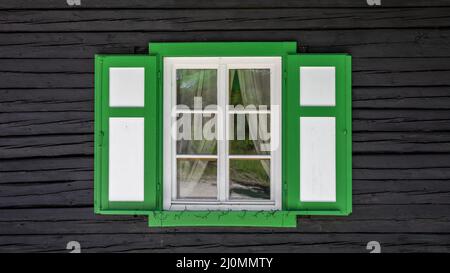Ancienne fenêtre ancienne en bois blanc vintage avec contour vert et volets sur un mur en bois brun.