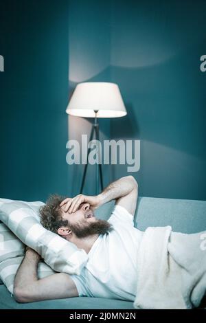 Le Caucasien veut dormir mais ne peut pas à cause de voisins bruyants. L'homme fatigué se trouve dans son lit et ses yawns. Gros plan. Arrière de la chambre Banque D'Images