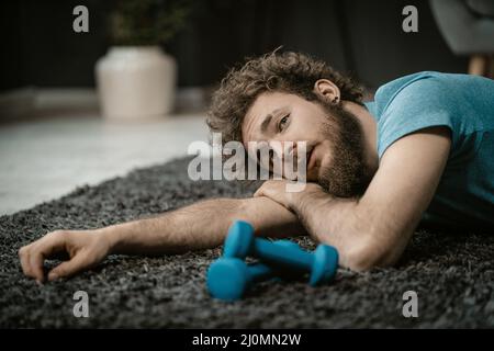 Un homme épuisé après un entraînement dur se trouve fatigué sur le sol à côté des haltères. Paresseux Guy ne veut pas faire du sport, manque d'énergie Banque D'Images
