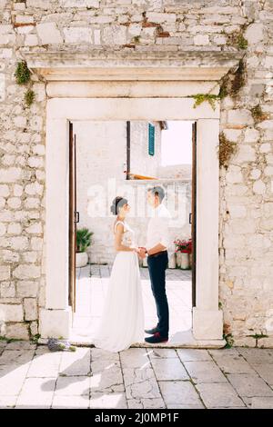 Sibenik, Croatie - 05.06.17: Marié et mariée dans un stand de robe en dentelle blanche à l'entrée de l'ancien bâtiment tenant les mains Banque D'Images