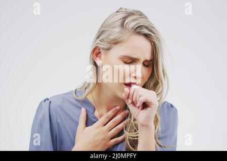 Elle déteste être malade. Photo en studio d'une jeune femme attractive toussant sur fond gris. Banque D'Images