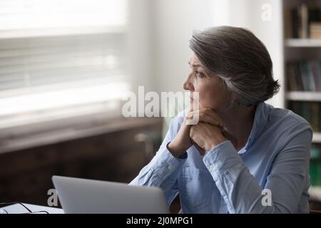 Femme d'affaires sérieuse pensive et âgée distraite du travail en regardant la fenêtre Banque D'Images