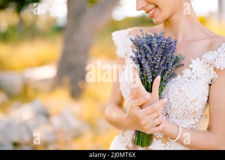Sibenik, Croatie - 05.06.17: Mariée souriante avec un anneau et un bracelet perle sur sa main dans une robe de dentelle blanche presse un bouquet Banque D'Images