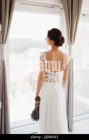 Sibenik, Croatie - 05.06.17: Mariée dans une robe de dentelle blanche se tient près de la fenêtre avec un bouquet de lavande et regarde dans le di Banque D'Images