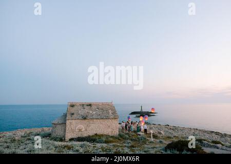 Sibenik, Croatie - 05.06.17: Des jeunes mariés avec des invités lancent des lanternes chinoises depuis le cap Punta Planca, debout près d'un ancien chur Banque D'Images