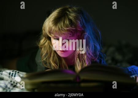 Enfant lisant un livre magique au lit. Enfant garçon lit des livres à la maison. Enfance heureuse, enfant rêvant. Banque D'Images