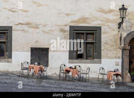 Ancienne fenêtre sombre avec tables rondes noires et chaises en métal sur la chaussée en pierre. Banque D'Images