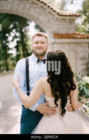 La mariée embrasse le marié dans le parc à côté d'une belle arche de brique, vue arrière Banque D'Images