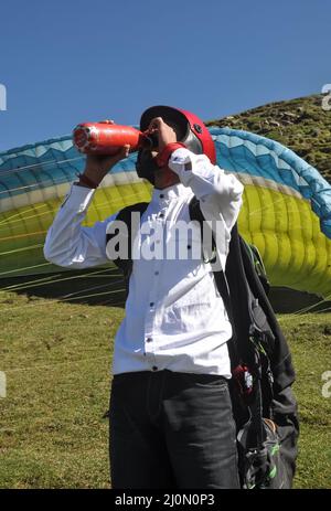 Un jeune homme boit de l'eau avec une bouteille avant de prendre un vol en parapente dans la montagne Banque D'Images