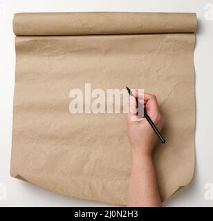 La main femelle tient un crayon de bois sur un rouleau de papier brun sur une table blanche. Place pour écrire du texte, liste Banque D'Images