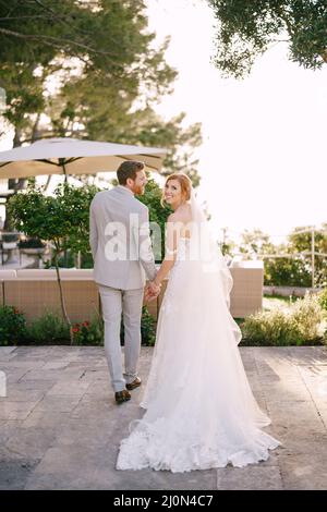 La mariée et le marié tiennent les mains tout en se tenant près des fauteuils sous un parasol du soleil Banque D'Images