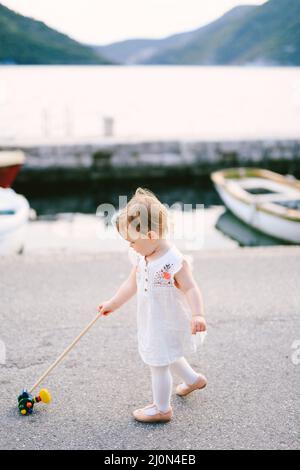 Une petite fille marche le long de la jetée avec un jouet sur fond de mer, de montagnes et de bateaux garés Banque D'Images