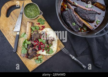 Les côtes de bœuf braisées traditionnelles à la sauce au vin rouge et au chimichurri ont servi de vue de dessus dans un four hollandais au design moderne Banque D'Images