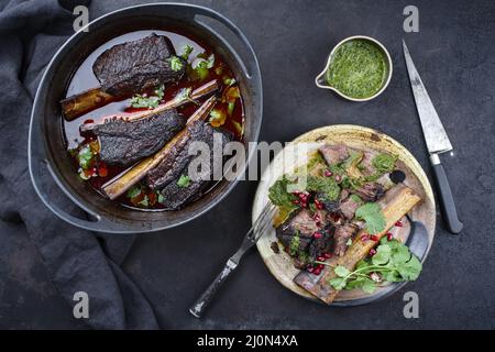 Les côtes de bœuf braisées traditionnelles à la sauce au vin rouge et au chimichurri ont servi de vue de dessus dans un four hollandais au design moderne Banque D'Images