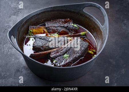 Côtelettes de bœuf braisées traditionnelles à la sauce au vin rouge servies en gros plan dans un four hollandais au design moderne Banque D'Images