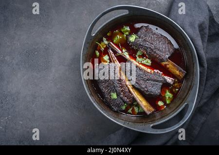 Les côtes de bœuf braisées traditionnelles à la sauce au vin rouge sont servies en gros plan dans un four hollandais au design moderne avec espace de copie laissé Banque D'Images