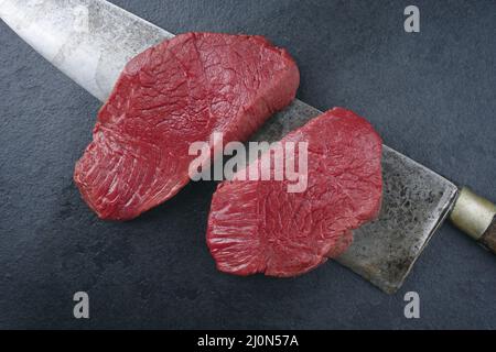 Morceau de steak et tranches de bœuf de bison vieilli et sec brut comme vue de dessus sur fond noir avec un grand couteau Banque D'Images