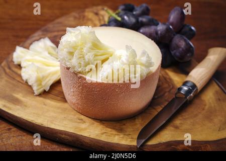 La tete de moine traditionnelle, fromage de montagne des Alpes, servi avec des raisins sur une planche de bois Banque D'Images