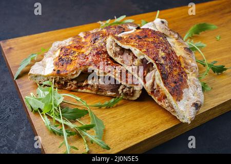 Pizza italienne traditionnelle calzone avec thon et oignons servi en gros plan sur un panneau en bois Banque D'Images