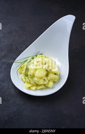 Salade de pommes de terre allemande traditionnelle avec oignon et ciboulette servie en gros plan dans un bol design sur un tableau noir rustique Banque D'Images