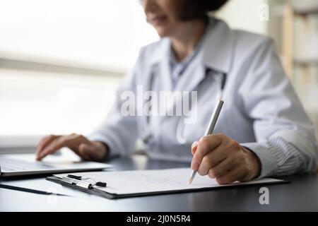Mains d'une femme médecin mature remplissant des dossiers médicaux papier Banque D'Images