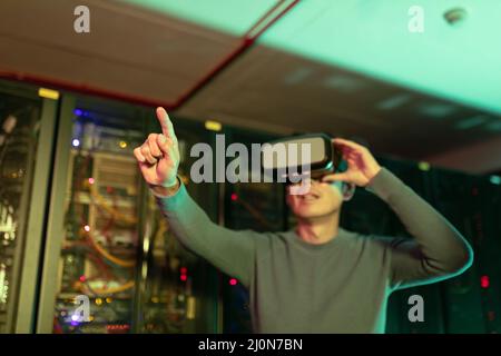 Homme asiatique portant un casque vr touchant un écran invisible dans la salle des serveurs informatiques Banque D'Images